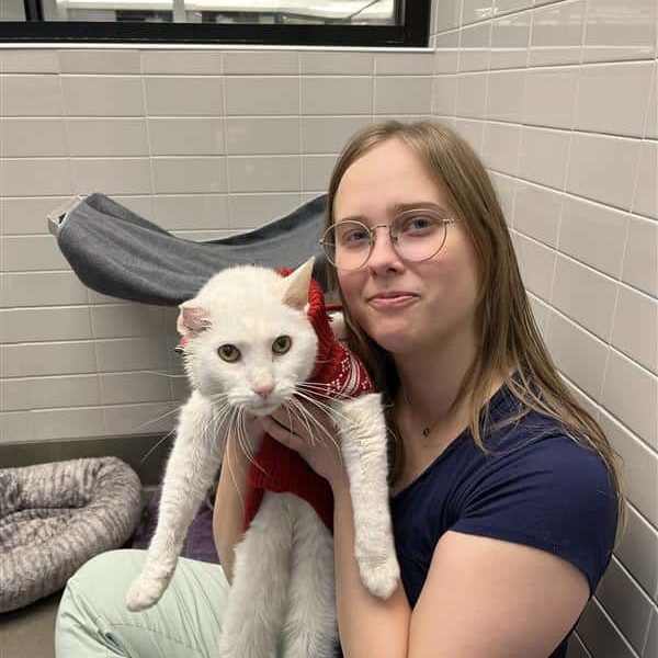 Laurel, an NHS employee, posing with a white cat in a cat room