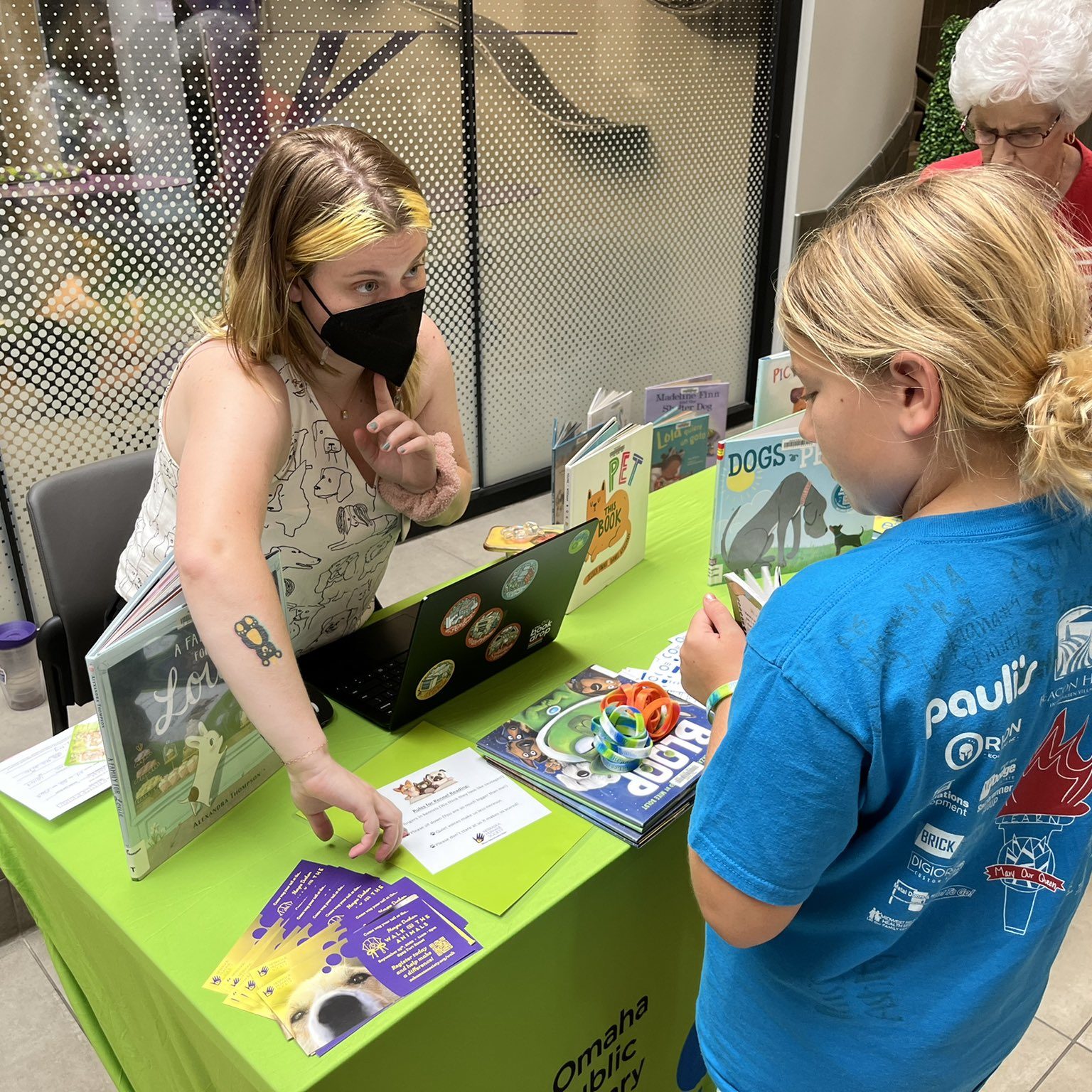 Elly the librarian showing a young girl a book so she can read to pets at NHS
